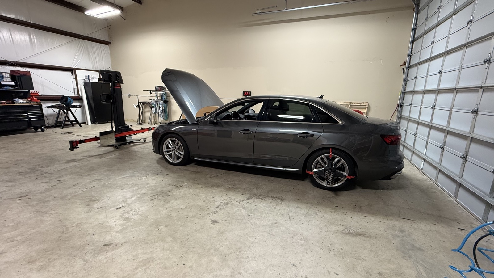 Gray Audi A4 with its hood up, staged beside the ADAS calibration frame and wheel targets in the air-conditioned South Texas Auto Glass shop in Corpus Christi, TX